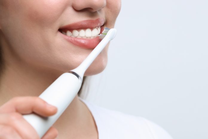 woman,brushing,her,teeth,with,electric,toothbrush,on,white,background,